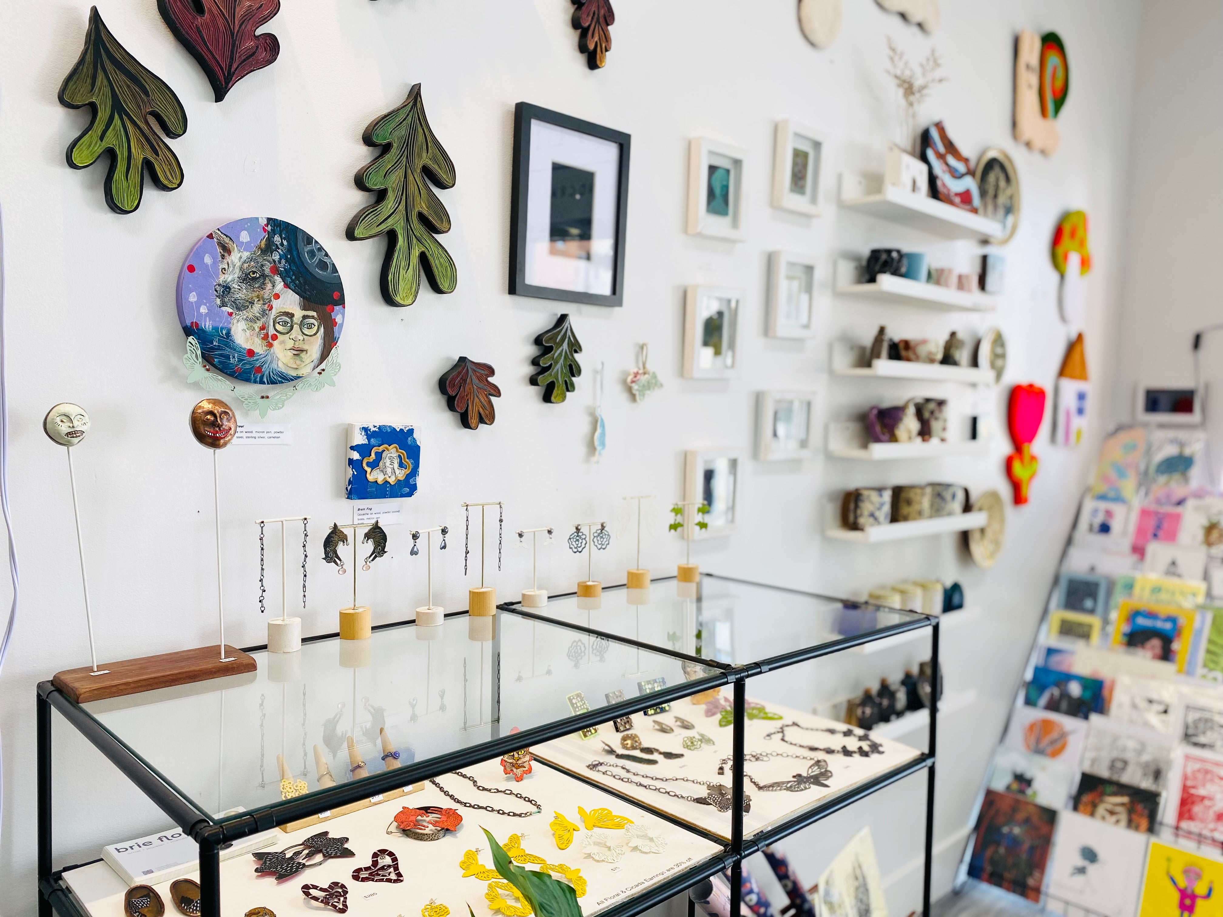 A view of a wall in our storefront gallery of paintings, prints, jewelry, and more!